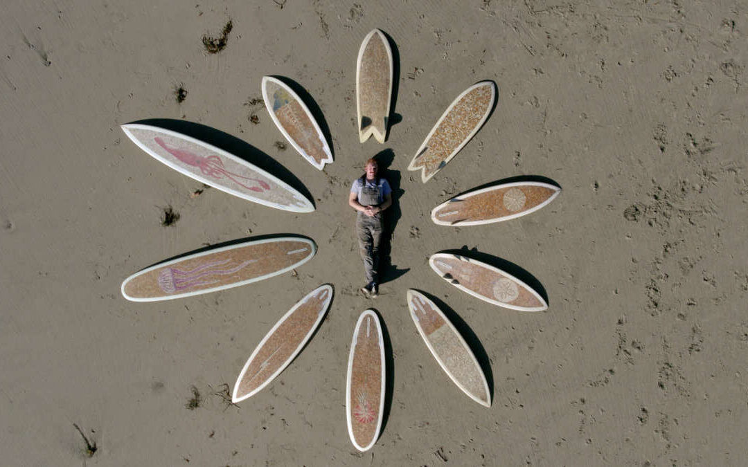 A man lies on the beach with cigarette surfboards place around him in a circle.